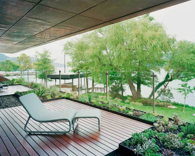 A modern balcony, surrounded by green plants, is even more exposed to the natural world right in front of the house with the use of glass panels.
