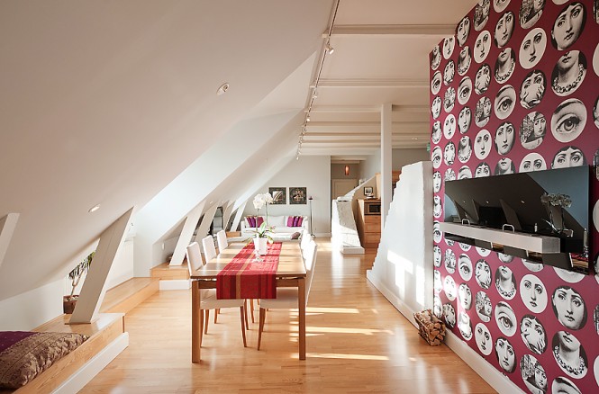 The tallest wall in the centre of the apartment has been adorned with the eye-catching red and white Fornasetti faces design of  Teme e Variazioni wallpaper, from Cole & Son; decorating the tallest wall in the attic space draws the room proportions upwards, combating the feeling that the space closes in.