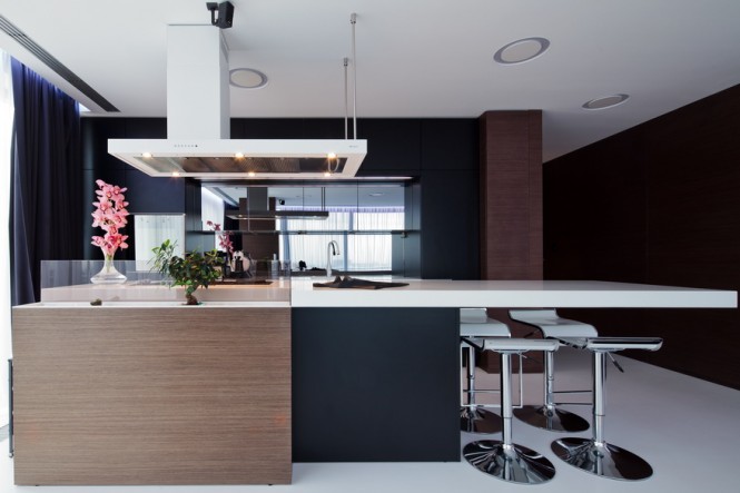 The kitchen area is backed by mirrored panels to reflect the large windows on opposite side, bouncing light around the deeper part of the layout. An asymmetrical white extractor echoes the shape of the white Corian countertop that protrudes long past the kitchen cabinetry to provide a dining area, and a tiny touch of stylish whimsy, in the form of a glazed mini courtyard, sits right in the central island, forming an unusual splashback to the hob.