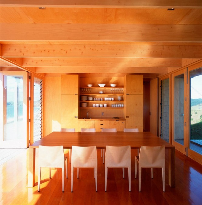 Sustainable, natural timber runs the length of the box-like structure, supported by sturdy struts, which makes the construction appear reminiscent of the rafter dams that were popular in this region at the turn of the last century. The boarded box opens up to reveal a simple interior layout, where the living room is free to soak up the sun and take in the tranquil location, a patch of cleared bush with an ocean view, where it takes on a campsite ambience.