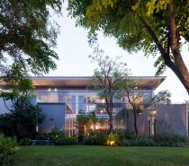 The modern house's exterior shows a boundless lawn filled with trees and greenery but no fences or walls.