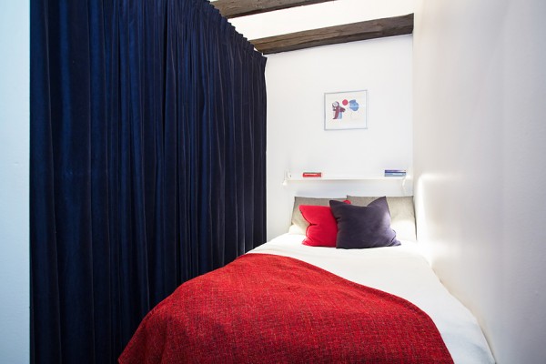 This snug bedroom solves the storage problem by concealing a spacious closet behind a velvet curtain.