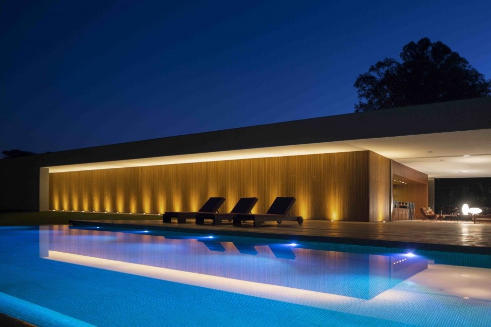 Marcio Kogan's Casa Lee Concrete House- exterior at night with view from  illuminated pool | Interior Design Ideas